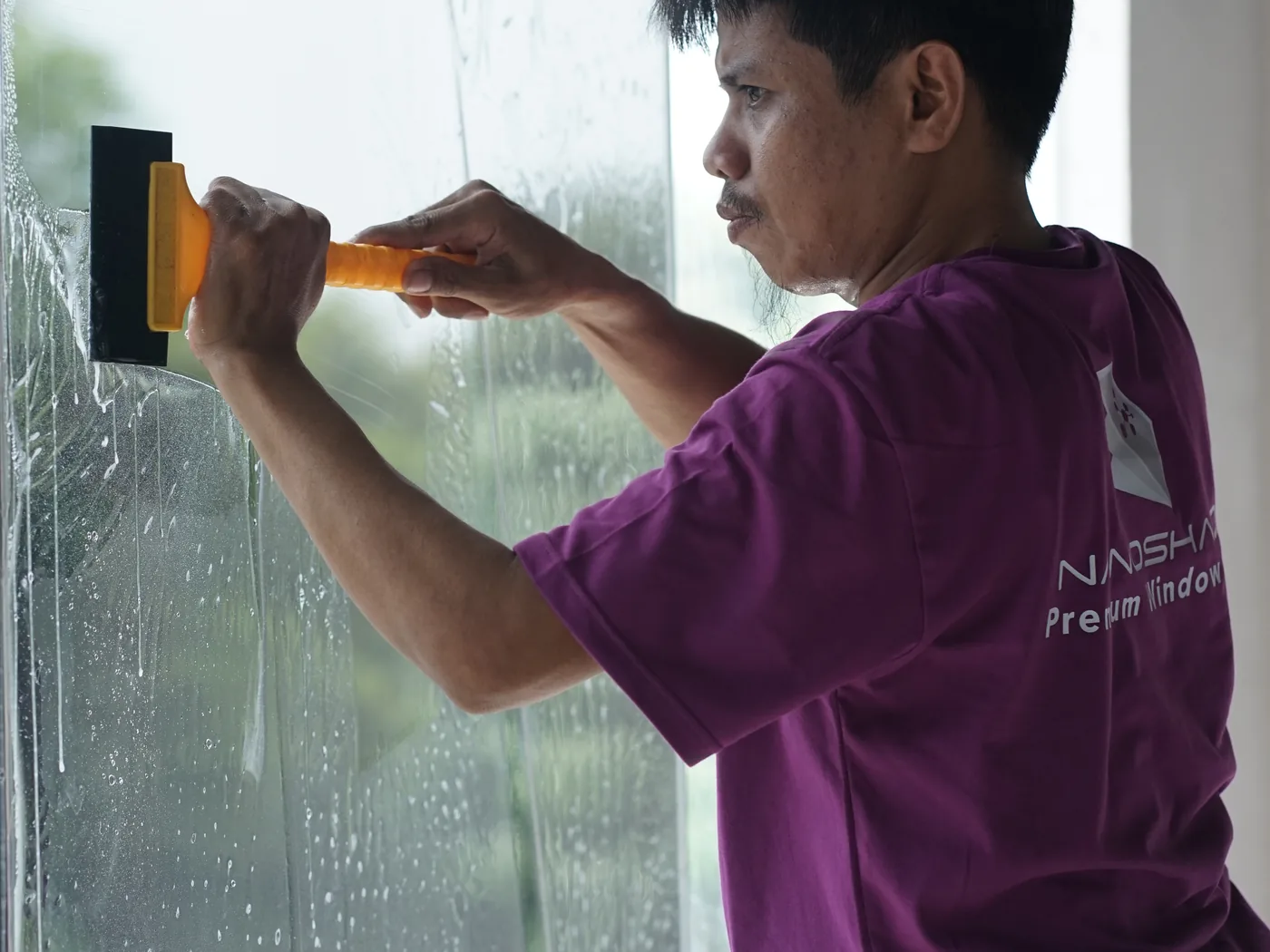 Tampak dekat teknisi NanoShade menarik squeegee kuning di atas film basah pada kaca
